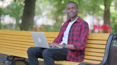 Laptop üzerinde çalışırken kameraya gülümseyen genç Afrikalı adam.