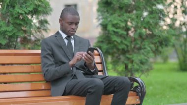 Afrikalı İşadamı Akıllı Telefonla Dışarda Bir Bankta Otururken Şok Oldu