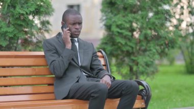 Bir bankta otururken Afrikalı İşadamı telefonda tartışıyor.