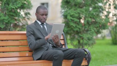 Bir bankta otururken Tablet 'te Başarı Kutlaması yapan Afrikalı İşadamı