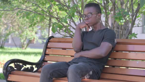 Schlafen Junger Afrikaner Sitzt Draußen Auf Bank — Stockvideo