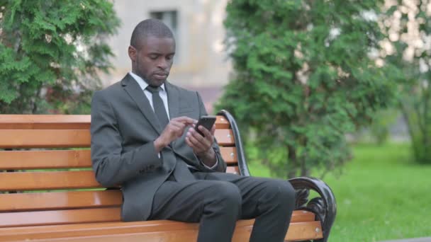 Африканський Бізнесмен Перегляд Смартфона Сидячи Відкритому Повітрі — стокове відео