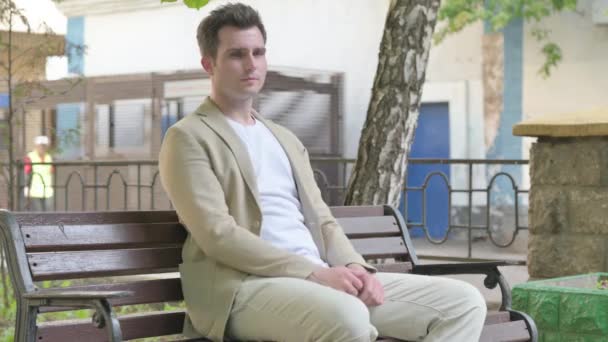 Hustender Junger Mann Sitzt Draußen — Stockvideo