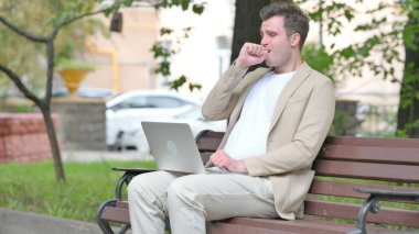 Laptop kullanan sıradan bir genç adam öksürüyor.