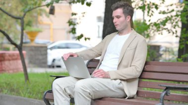 Dizüstü bilgisayarla çalıştıktan sonra sıradan bir genç adam Bench 'i açık havada bırakıyor.
