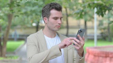 Casual Young Man Browsing Internet on Smartphone Outdoor