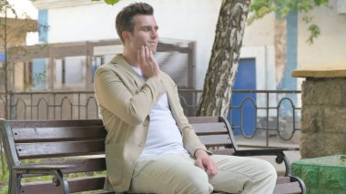 Dişi ağrıyan genç adam dışarıda oturuyor.