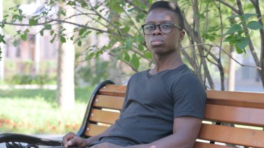 Dışarıda oturan ve kameraya bakan Ciddi Afrikalı Genç Adam