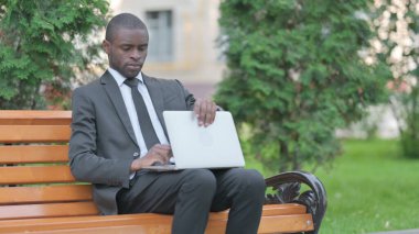 Afrikalı İşadamı Bench 'te laptopta geliyor, oturuyor ve çalışıyor.