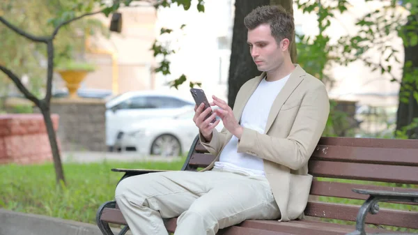 Lässiger Junger Mann Benutzt Smartphone Während Draußen Auf Einer Bank — Stockfoto