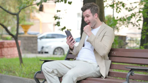 Jovem Casual Comemorando Sucesso Smartphone Enquanto Sentado Livre Banco — Fotografia de Stock