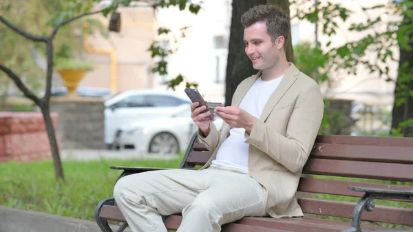 Casual Jovem Fazendo Compras Line Telefone Enquanto Sentado Livre — Fotografia de Stock