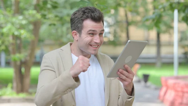 Casual Young Man Celebrating Success on Tablet Outdoor