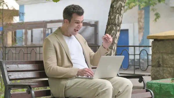 Excited Young Man Celebrating Success on Laptop Outdoor