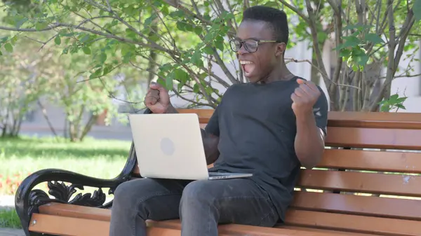 Excited Young African Man Celebrating Success on Laptop Outdoor