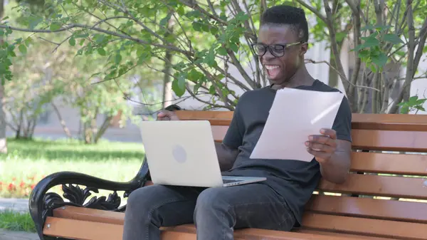 Young African Man Celebrating while Working on Laptop and Documents Outdoor