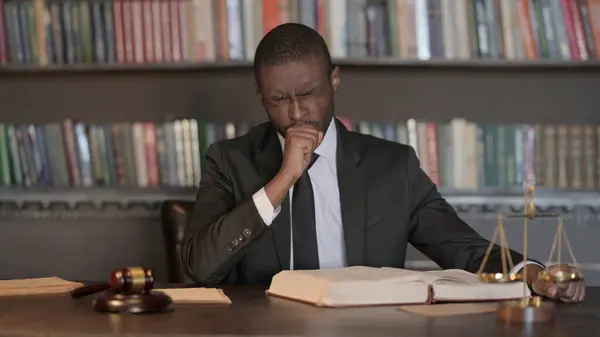Sick African Male Lawyer Coughing while Reading in Office