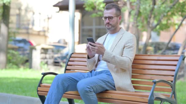 Středověký Muž Pomocí Smartphone Zatímco Sedí Venku Lavičce — Stock video
