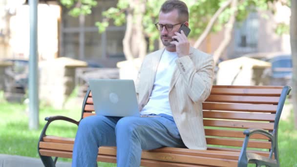 Μεσήλικας Άντρας Που Μιλάει Στο Τηλέφωνο Και Χρησιμοποιεί Laptop Outdoor — Αρχείο Βίντεο