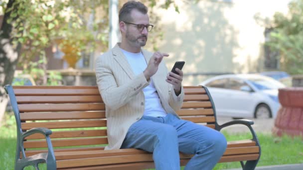 现代休闲男人坐在户外的长椅上 一边用智能手机庆祝成功 — 图库视频影像