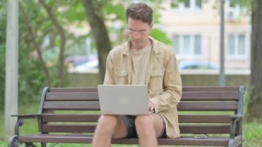 Dışarıda otururken Sırt Ağrısı Olan Gündelik Genç Adam Dizüstü Bilgisayarı Kullanıyor