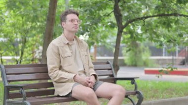 Başağrısı olan modern genç adam Bench 'te oturuyor.