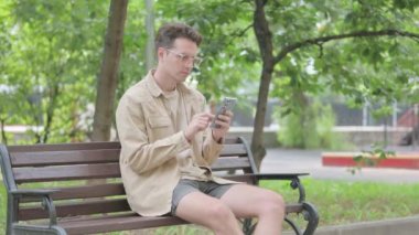 Modern Genç Adam Bench 'te otururken Smartphone kullanıyor.