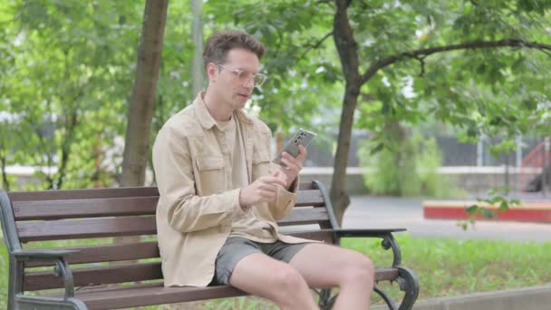 Nowoczesny Młody Człowiek Rozmawia Przez Telefon Siedząc Ławce — Wideo stockowe