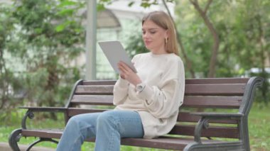 Bir bankta otururken tablet kullanan sıradan bir genç kadın.