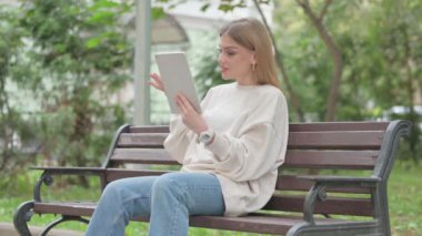 Bir bankta otururken Tablet 'te görüntülü sohbet yapan sıradan bir genç kadın.