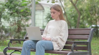 Laptop üzerinde çalışırken kameraya gülümseyen sıradan bir genç kadın.