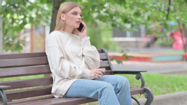 ベンチに座って電話で話す若い女性 — ストック動画