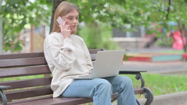 Mujer Joven Hablando Por Teléfono Utilizando Ordenador Portátil Aire Libre — Vídeo de stock