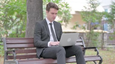 Baş ağrısı olan genç iş adamı laptopla dışarıda çalışıyor.