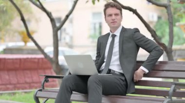 İşadamı Bench 'te otururken Sırt Ağrısı Olan Dizüstü Bilgisayarı Kullanıyor