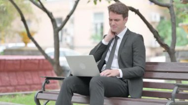 Boyun ağrısı olan bir iş adamı laptopla dışarıda çalışıyor.