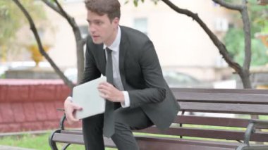 İşadamı geliyor, bankta oturuyor ve laptopta çalışıyor.