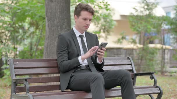 Młody Biznesmen Zszokowany Stratą Telefonu Podczas Siedzenia Zewnątrz Ławce — Wideo stockowe