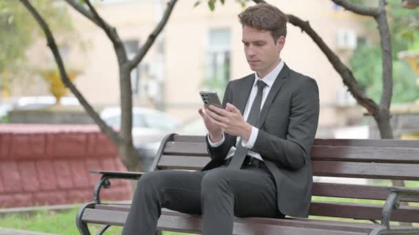 Biznesmen Świętuje Sukces Online Telefonie Podczas Siedzenia Ławce — Wideo stockowe