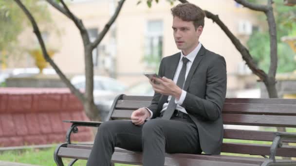 Επιχειρηματίας Μιλάει Στο Τηλέφωνο Ενώ Κάθεται Στο Bench — Αρχείο Βίντεο