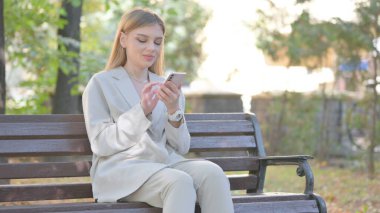 Genç İşadamı Bench 'te otururken telefonu kullanıyor.