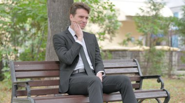 Diş ağrısı olan genç iş adamı dışarıda oturuyor.