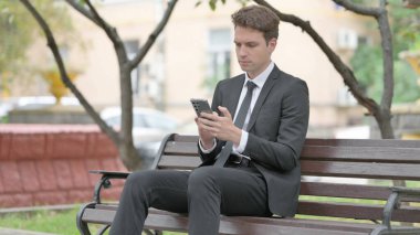 Businessman using Phone while Sitting on Bench