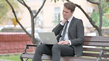 Boyun ağrısı olan bir iş adamı laptopla dışarıda çalışıyor.