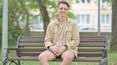 Dış mekan imzalanırken kameraya gülümseyen sıradan genç adam.