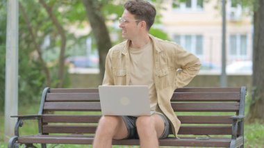 Dışarıda otururken Sırt Ağrısı Olan Gündelik Genç Adam Dizüstü Bilgisayarı Kullanıyor