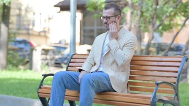 Diş ağrısı olan orta yaşlı bir adam dışarıda oturuyor.