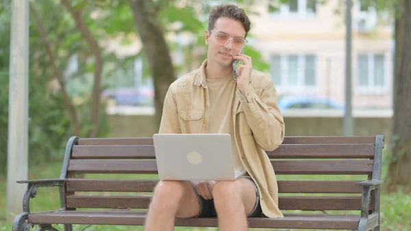 Случайный Молодой Человек Разговаривает Телефону Помощью Ноутбука Открытом Воздухе — стоковое фото