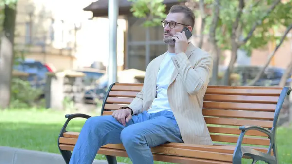 Orta Yaşlı Bir Adam Bankta Otururken Telefonla Konuşuyor — Stok fotoğraf