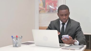 Dizüstü bilgisayarda çalışan ve akıllı telefon kullanan Afrikalı İşadamı
